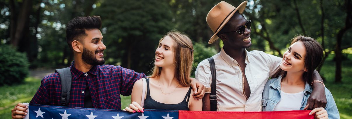 happy-four-students-relaxing-nature-with-american-flag-celebrating-4th-july-min