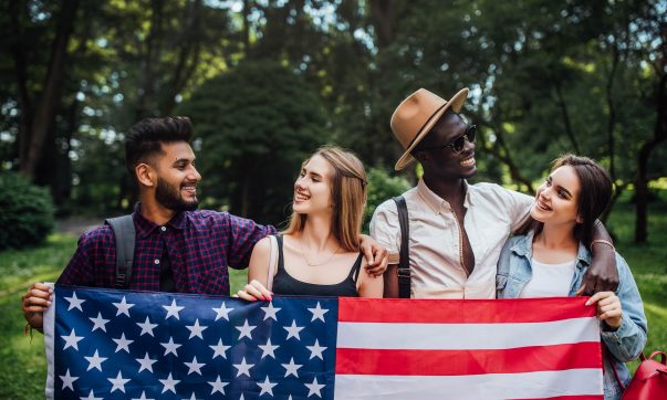 happy-four-students-relaxing-nature-with-american-flag-celebrating-4th-july-min