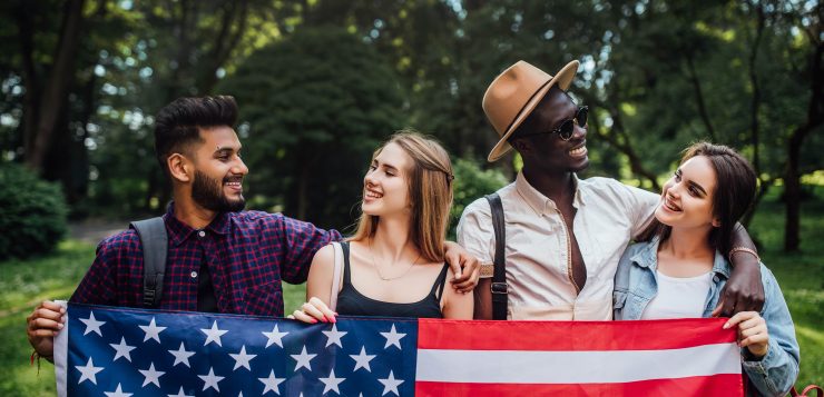 happy-four-students-relaxing-nature-with-american-flag-celebrating-4th-july-min
